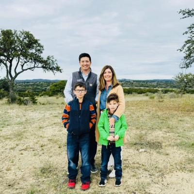A husband and wife with their two sons smiling while standing in a field.