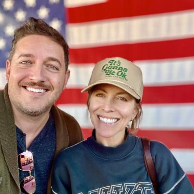 2 people standing smiling in front of an American Flag