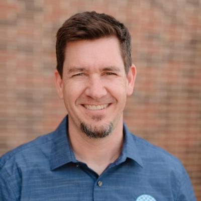 Man smiling at the camera in front of a brick wall.