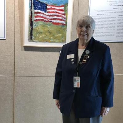 A woman in a navy blazer in front of a painting of an American flag.