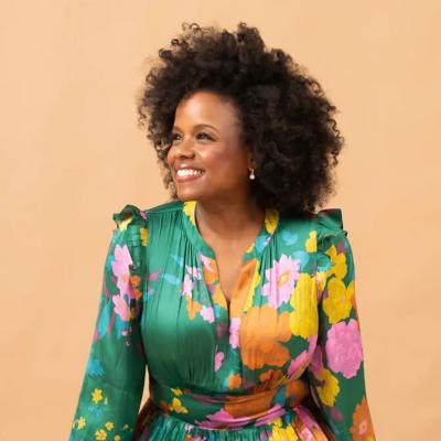 Woman in a green floral dress sitting and smiling while looking to the left.