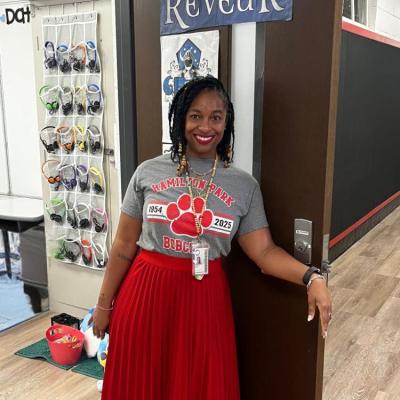 A woman standing in a doorway wearing a red skirt and a grey tshirt.