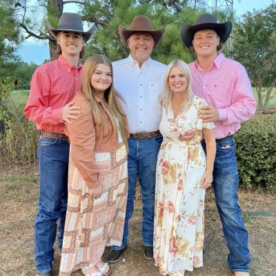 A family of five poses outdoors, dressed in western attire with cowboy hats and boots.