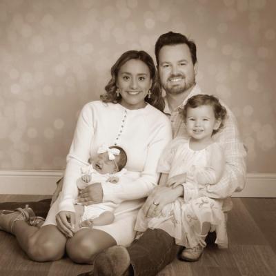 Husband, wife, toddler, and baby sitting smiling in a sepia portrait.