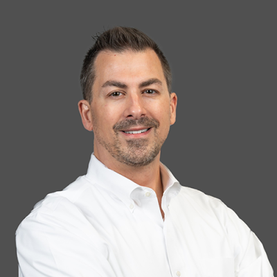 A man in a white button down standing against a grey background