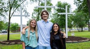 a boy with his arms around two girls infront of three crosses