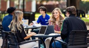 Students sitting at tables talking and studying with laptops and textbooks.