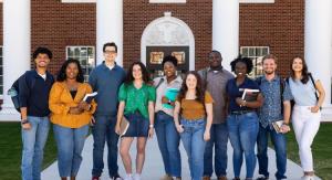 Group of male and female students smiling at the camera in front of a brick academic building with white columns.