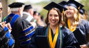 A woman in a navy cap and gown walking in a line of graduates.