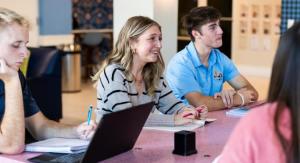 A female student holding a pink pen while she chats with her peers at a table