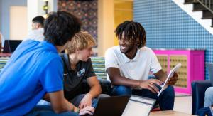  Three students collaborate with laptops in a casual lounge area, engaging in discussion and sharing ideas.