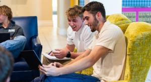 Two males sit in colorful chairs looking at a laptop smiling.
