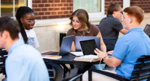 Three students sitting around a table while they work on their laptops.