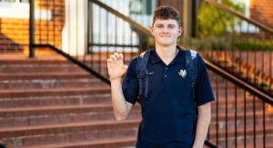 A boy in a blue nike ETBU shirt holding up a tiger paw hand symbol infront of stairs