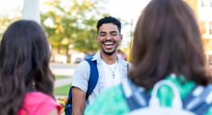A group of college students interacting and smiling outdoors on campus.