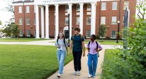 3 people walking down a concrete path with a large building in the background