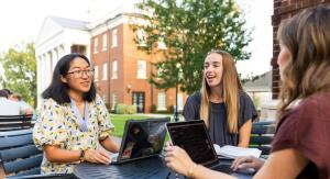 3 people sitting at a table together talking with laptops