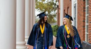Two females in navy regalia walking on a red brick building porch.
