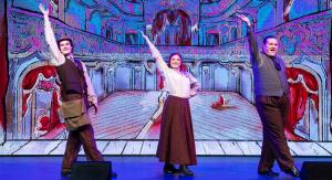 3 people on a stage with arms raised in formal clothing