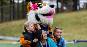 Children smiling with Tabby the Tiger mascot outside on a football field