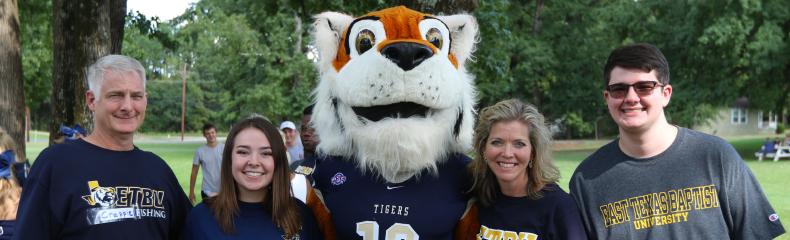 A group of five people stands outdoors with a tiger mascot.