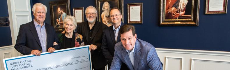 A group of people in formal attire standing around a large check being signed