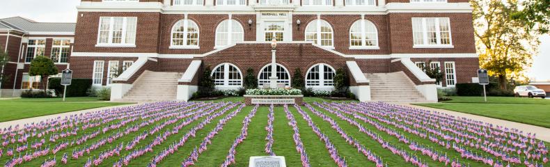 A large brick building with white columns and many small American flags on the lawn.