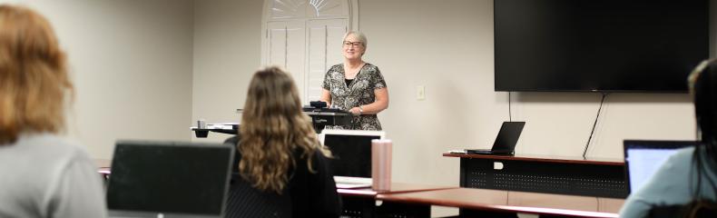 Classroom setting with attendees facing a speaker at a podium.