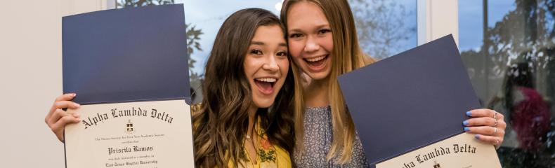 Two women smiling at the camera holding up awards in their hands