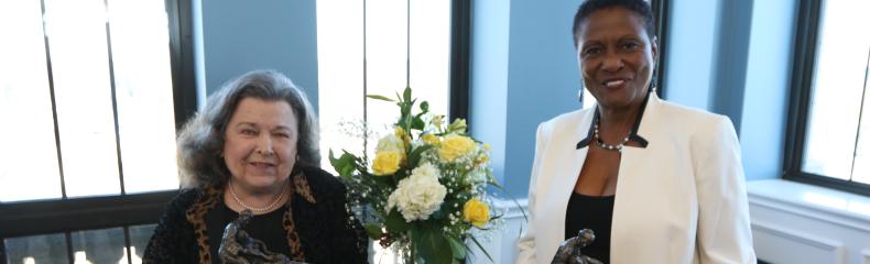 Two women smiling at the camera with awards in their hands in front of a table