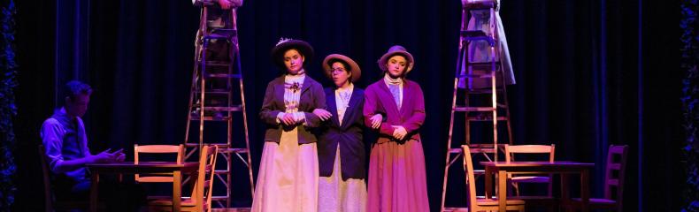 Performers in period costumes on stage with ladders and purple lighting