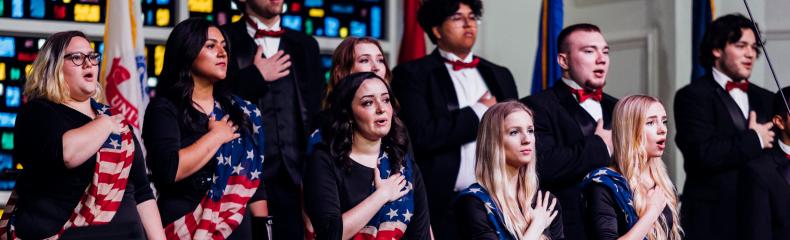 Choir students with their hands over their hearts with American Flag sashes on