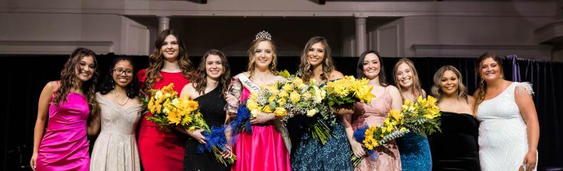 A group of women in ballgowns smiling at the camera on stage