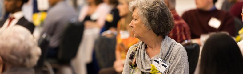 Picture of older lady looking towards the stage at a table with people in the background