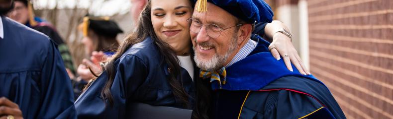 A man and a women embracing each other smiling in their graduation regalia 