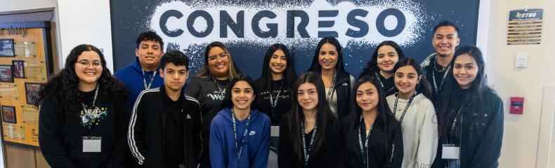 Group of students standing in front of event banner smiling at the camera 