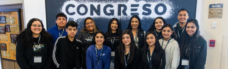 Group of students standing in front of event banner smiling at the camera 