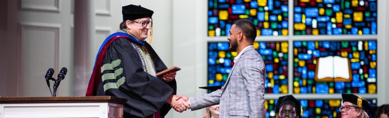 Tiger mascot holds a smiling girl in a yellow outfit, surrounded by excited children near a sports field.