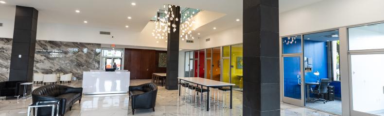  Modern lobby with glossy white marble floor, black leather seating, colorful paneling, and glass-walled office.