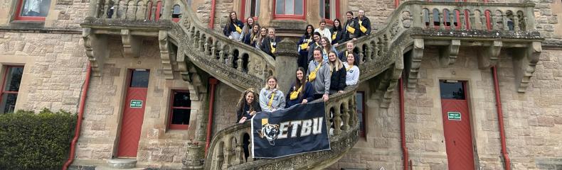 A group of people on stairs in front of a large old stone building holding a banner that says "ETBU".