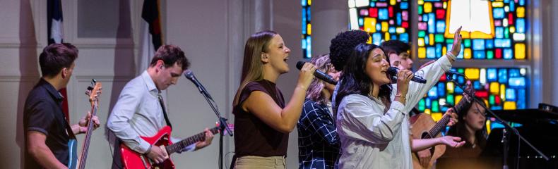 Male and females singing on stage in a chapel