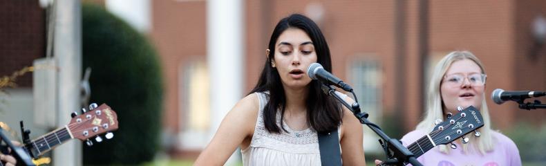 Woman singing and playing guitar with woman singing in the background