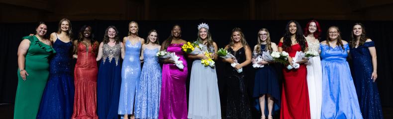 A group of women in ballgowns smiling at the camera on stage