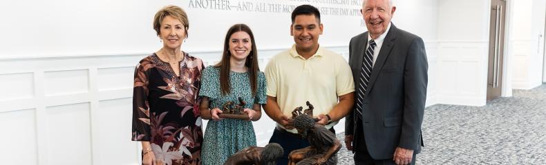 Two males and females standing in front of a table with a navy ETBU tablecloth and Jesus feet washing statue on the top of the table