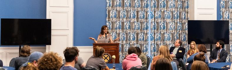 A woman speaking behind a podium to a room full of people.