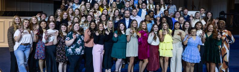 Large group of male and female students holding their graduation rings smiling at the camera 