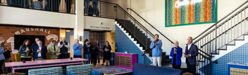 Men speaking in front of crowd in residential hall lobby 