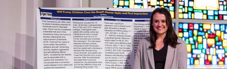 Student stands with research project poster board in front of a stained glass window