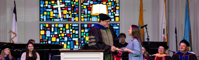 Student shakes hand of professor on stage and she receives a 2024 Academic Excellence Award