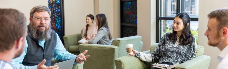 Faculty member sits in a common area conversing with students